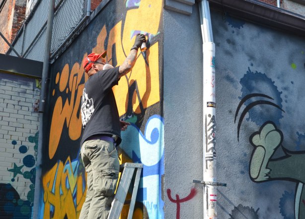 Graffiti Alley - man on ladder spray painting a street art piece