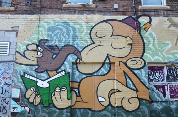 Mural of a large monkey sitting, holding a green book with his feet and smoking a pipe using one of his hands. 