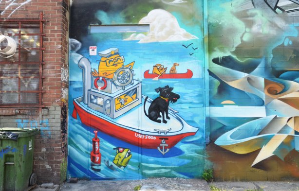Graffiti Alley - uber5000 mural of a boating scene, yellow bird sterring a boat, black dog sitting on the bow, another yellow bird paddling a red canoe