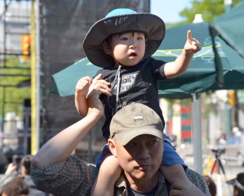 A young Asian boy sits on his father's shoulders