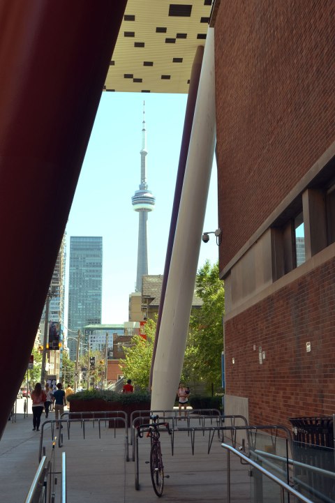 Looking through the pencil like supports to the black and white upper lever addition to OCAD (Ontario College of Art and Design). The CN TOwer and other tall toronto buildings are in the background. 