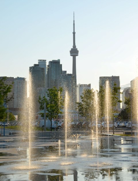 Sherbourne Common looking towards downtown and the CN tower. Splash pad with fountains in the foreground with late afternoon sun shining on the water