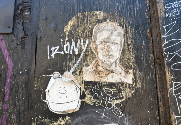 two wheatpaste graffiti pieces, one yipyaps and one man's head.  The word irony is written as well.  They are on a worn black painted wood surface