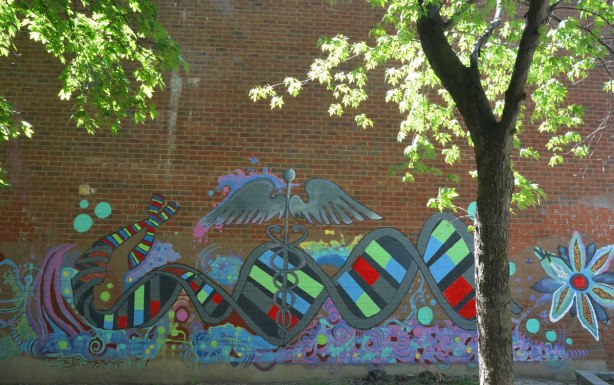 mural behind a small tree on a red brick wall, spiral of DNA, medical symbols, butterfly