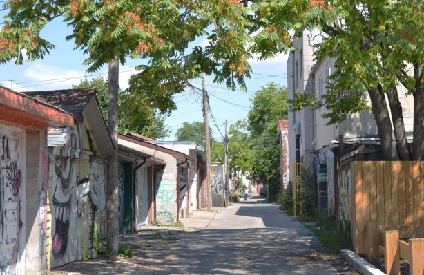 An alley that runs parallel to Ossington Ave., looking north with garages on both sides and a tree overhead, looking towards Humbert St.
