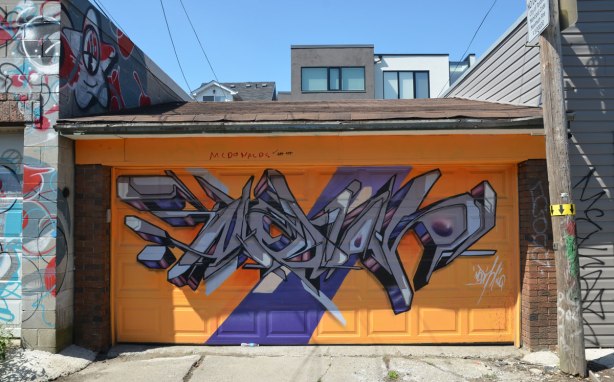 garage door painted orange and then a geometric street art painting in greys and purples painted on that