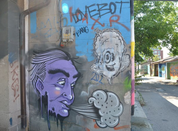 A purple faced man is blowing grey clouds, the alley is in the background. 