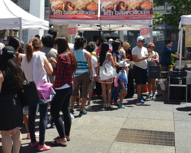 a longline of people waits for food at an outdoor festival at Yonge Dundas Square in Toronto