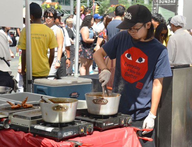 a young man preparing food outdoors on hotplates at a festival