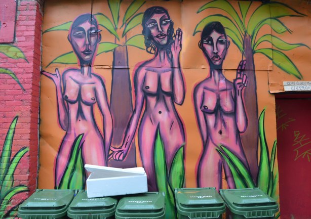 mural street art painting of a naked woman, three pink women standing together, drawn with purple outlines, on a pink background, with some green plants in the painting too 