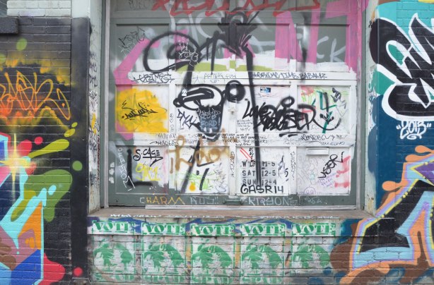 A black poser bunny spray painted on a wall that is covered with slaps, stickers, and words written in black marker