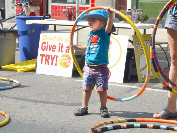 A young boy is playing with a hula hoop in front of a sign that says Give It a Try