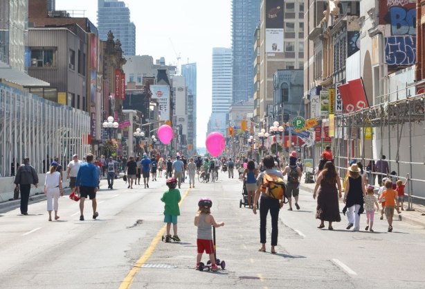 looking south on Yonge St. from Bloor street on a morning when no cars allowed. There are people walking on the street. There are also two kids with pink balloons. 