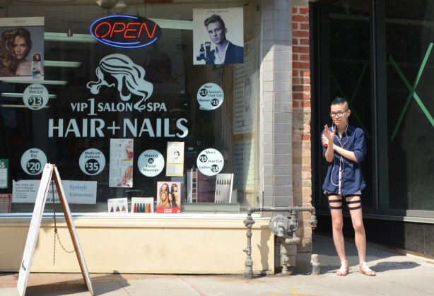 A young man is standing in a doorway beside a hair and nails shop on Yonge Street. 