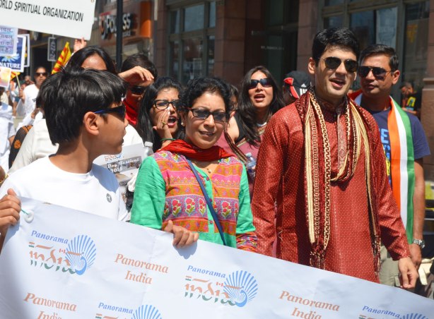 A group of people are walking in an India independence day celebration parade, they are holding a banner and walking behind it.