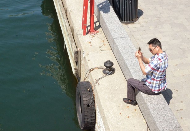 A young man poses as he sits on the barrier beside Lake Ontario