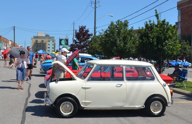 picture taken at a car show - An old British, original mini, white, is parked in a line of other other cars at a car show.