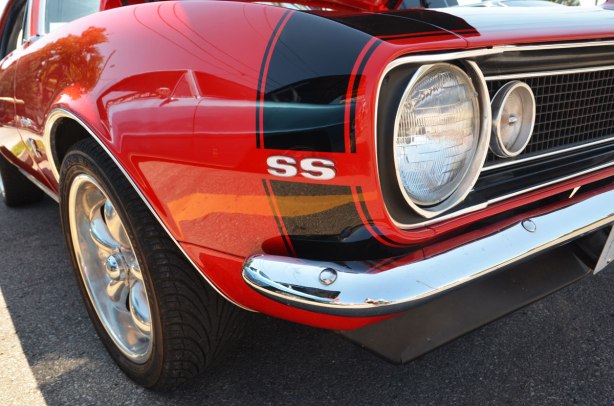 picture taken at a car show - the front corner of a red sports car showing wheel and front head lamps