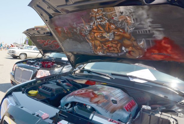picture taken at a car show - two black cars with their front hoods up showing the paintings that have been done under the hood