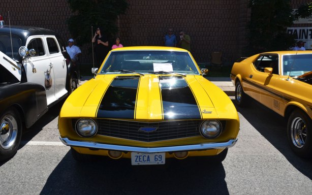 picture taken at a car show - Yellow 1969 Camaro car with two black stripes down the front hood.