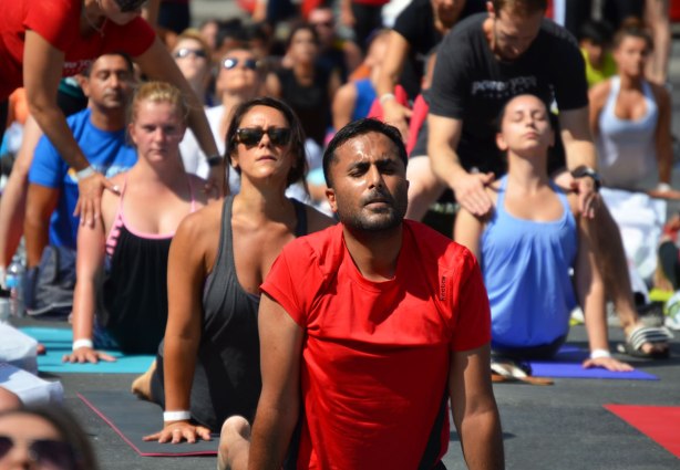 men and women at a yogathon - doing yoga outside in a large group, in downward dog position