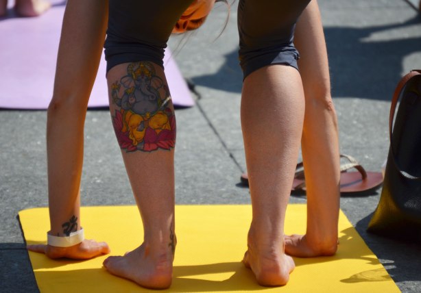men and women at a yogathon - doing yoga outside in a large group, woman with ganesha tattoo on her calf 