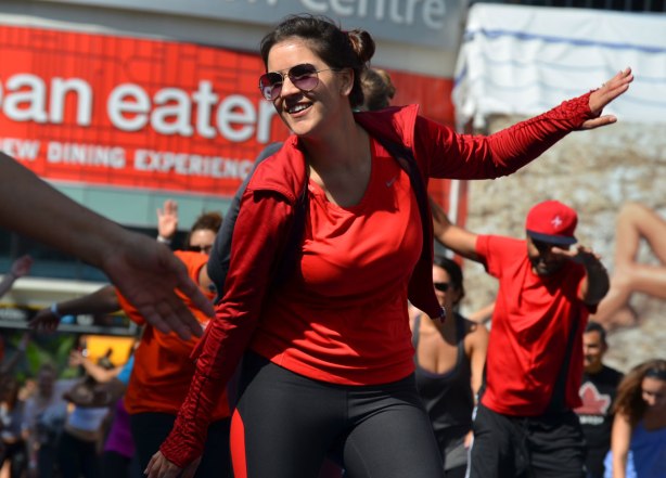 men and women at a yogathon - doing yoga outside in a large group, warming up to dance music, swinging arms
