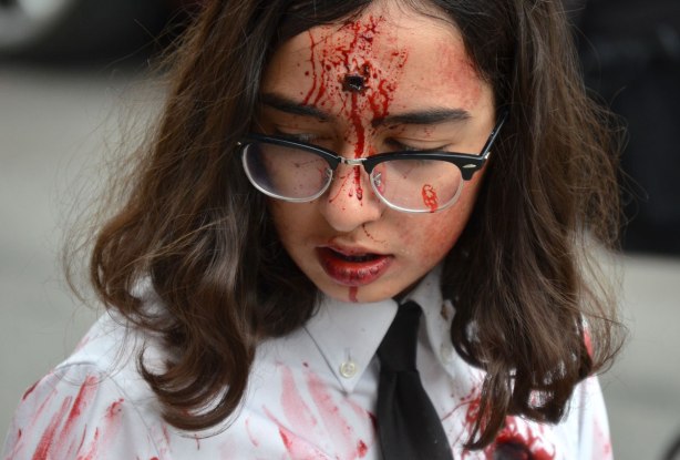 people dressed up as zombies - a woman with long hair and glasses, wearing a white shirt and black tie, with a bullet hole in her head. 