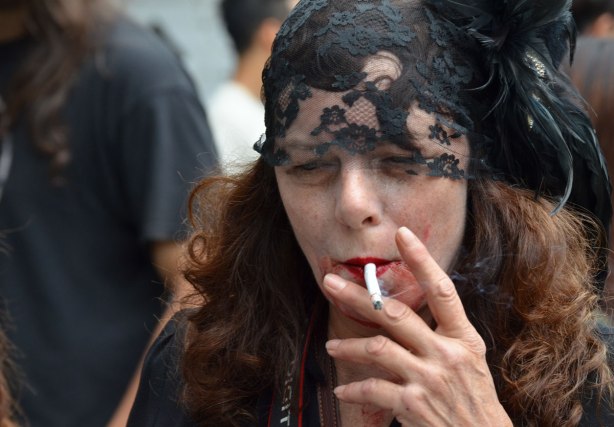 people dressed up as zombies - a woman with a black head scarf over the top of head and forehaed. She has long auborn hair and she's smoking a cigarette 