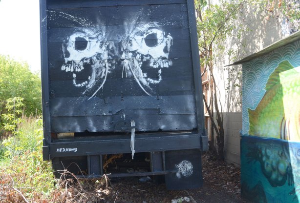 on the back of a truck, two white skulls with wide open mouths in profile, a raccoon and all signed by deadboy.