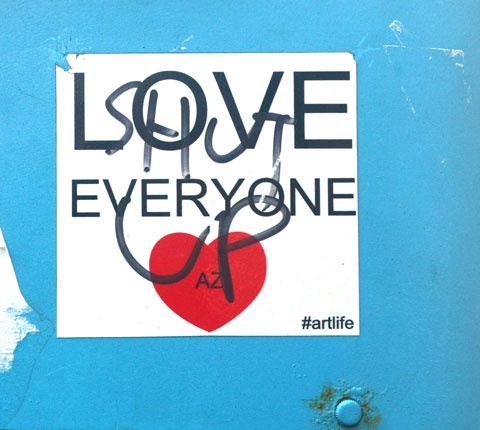 A sticker with a red heart and the words Love Everyone that someone has scrawled on in black marker, shut up