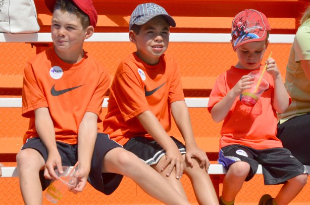 Three boys in orange T-shirts sitting on orange benches. A very orange picture