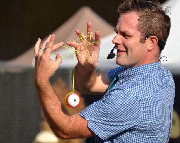 The Yo yo guy is doing a trick with a yo yo where he makes a shape out of the string and his fingers while the yo yo keeps spinning