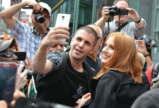 A group of fans in a crowd. One man is taking a selfie with the actress Jessica Chastain. Other people are taking photos of them. 