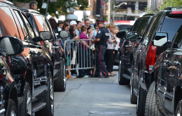 two lines of black Cadillac Escalades, looking down the lines to a group of people behind a barricade with a policeman standing with them. 