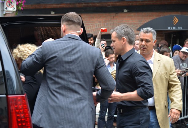 Matt Damon is directed towards a vehicle by a driver and a security guard. 