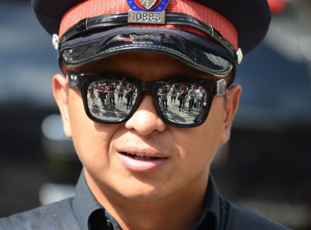 Close up of a policeman's face. He is wearing reflective sunglasses and the crowd is reflected in them. 