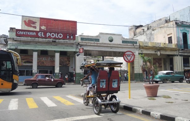 picture taken in the old part of the city of Havana Cuba -  the Cafeteria el Polo with it's red sign is across the street.  An old car is driving past, a bici (two passenger bicycle taxi) is also in the picture