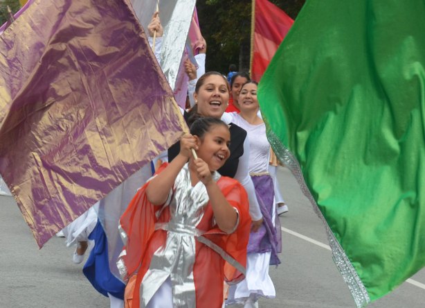 Some women are waving large coloured flags. A purple flag, and a green flag are the ones in the foreground. 