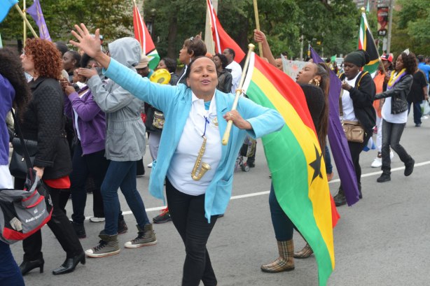 A woman poses with a red, yellow and green striped flag as she walks in a parade