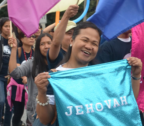 A woman is holding a shiny turquoise fabric sign with the word jehovah on it. 