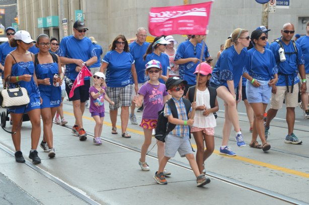 Four kids with flags walking in a labour day parade with their parents. 