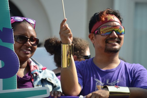 Two people in a labour day parade. The man is wearing wonder woman sunglasses. 