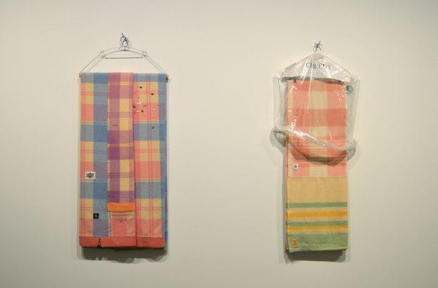 art installation at the Art Gallery of Ontario by Liz Magor - two hangers with plaid blankets folded over them hanging from hooks on a wall. One of the blankets has a clear plastic Creeds bag over the top part of it
