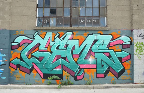 tag-like street art under a window in an alley that says GEMS