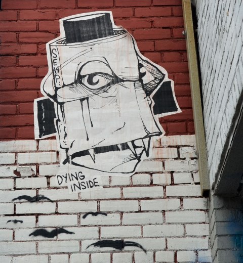 Wheatpaste high up on a wall, a large face like thing. The words 'dying inside' are part of the picture