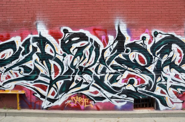 Black and white street art painting on a reddish brick wall, signed Jaroe