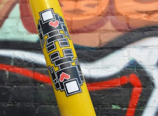 Two black lovebot robot stickers on a yellow protective sleeve around a cable that is helping to hold up a pole.