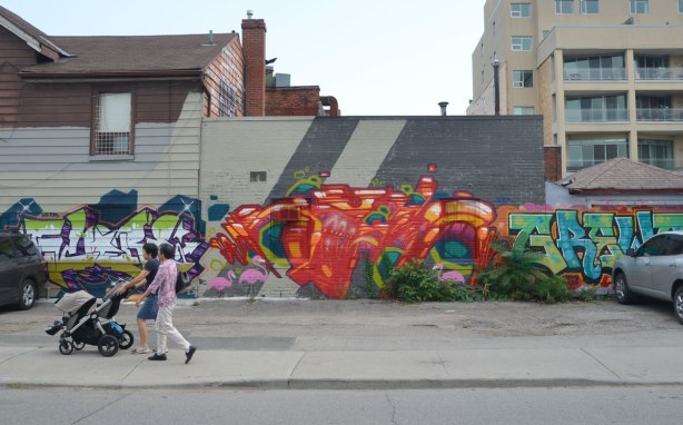 Two women pushing a stroller walk past some street art on Nassau St. in Toronto, a large orange piece ta