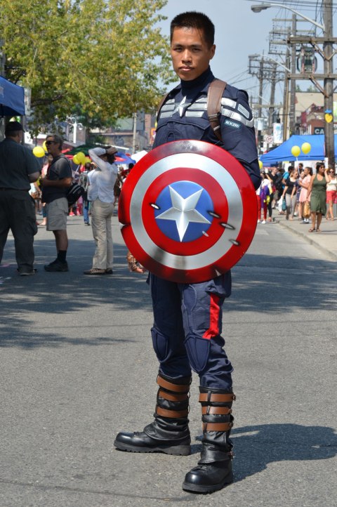 A young man with a Captain America shield, poses in the street 